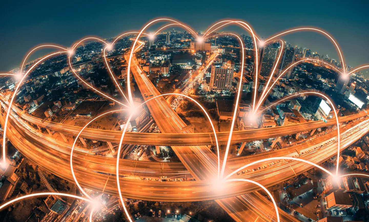 Aerial view of highways crisscrossing a city at night with light beams connecting from spot to spot like a technology network.
