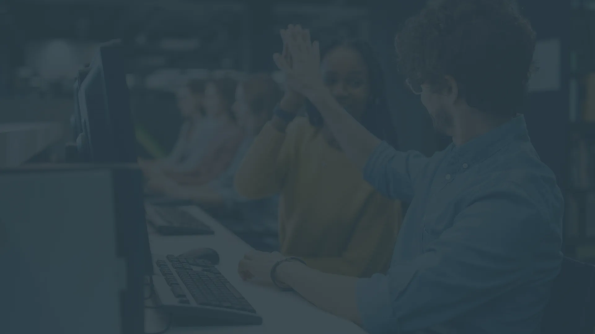 Two colleagues sitting in front of a computer giving each other a high-five.