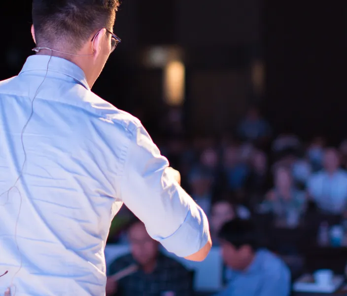 Person on stage with back to camera presenting to a crowd of people.
