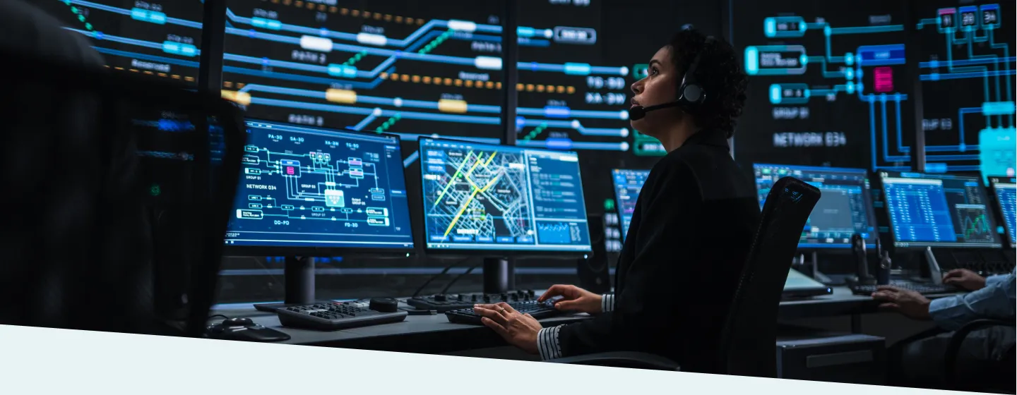 IT technical support specialist working on multiple digital screens with bright network maps in a monitoring control room.